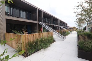 A multi-story residential building with balconies, a staircase, and a landscaped area with plants. - The Shoals Suites and Slips (Southold)