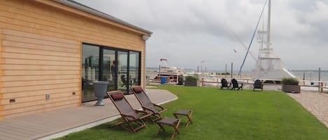 A deck with lounge chairs, a glass wall, and a view of the sea.