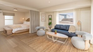 A modern hotel room with a bed, a sofa, a coffee table, and a view of the city. - The Shoals Suites and Slips (Southold)