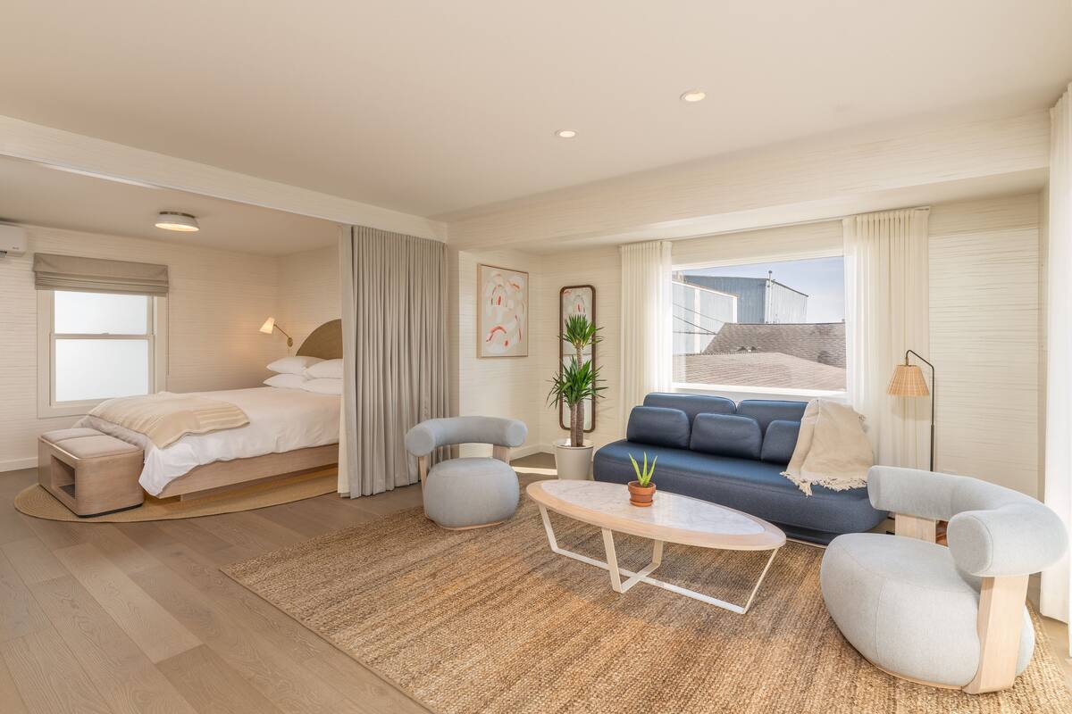 A modern hotel room with a bed, a sofa, a coffee table, and a view of the city.