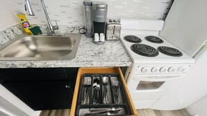 Una cocina con lavamanos, estufa y cajón con utensilios.