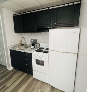 Une cuisine de taille réduite, avec des meubles de couleur sombre, un réfrigérateur blanc, une cuisinière à quatre brûleurs et une machine à café.