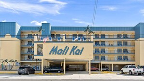A multi-story hotel named Mali Kai with a central entrance, parking area, and balconies on each floor.