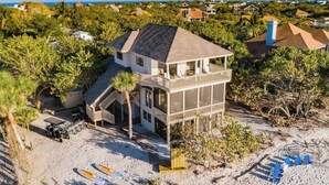 A beachfront property with a two-story house, a covered patio, and a sandy beach area with paddleboards. - Beachfront🌊3 KING suites & bunk room🛏️Pet Friendly🐾 (Captiva)