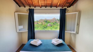 Una habitación con cama, dos toallas, una ventana con cortinas y vistas a un edificio.