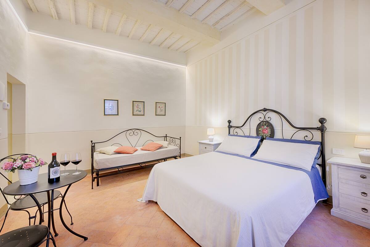 Une chambre à coucher avec un lit, des tables de chevet, une petite table avec une bouteille et des verres, et une chaise.