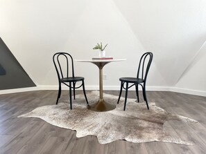 A room with a round table, two chairs, a small plant, and a cowhide rug.
