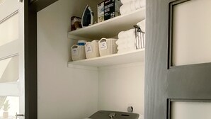 A laundry room with a front-loading washer and dryer, shelves above containing cleaning supplies, and a door with a handle. - Geo Dome - Unique Urban Getaway – one of a kind! (Springfield)