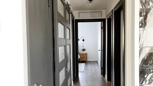 A hallway with a wooden floor, a door with a silver handle, and a wall-mounted light fixture. - Geo Dome - Unique Urban Getaway – one of a kind! (Springfield)
