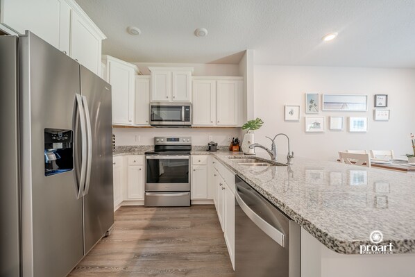 A modern kitchen with stainless steel appliances, white cabinetry, a granite countertop, and a backsplash.