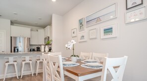 Une cuisine moderne avec des armoires blanches et des appareils en acier inoxydable. On y trouve un coin repas avec une table en bois et des chaises blanches.