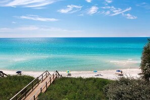 A beach with a wooden walkway leading to the shore, clear turquoise water, and a few beach umbrellas.