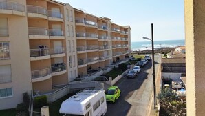 Un immeuble résidentiel à plusieurs étages, doté de balcons, donnant sur une rue et offrant une vue sur l’océan.
