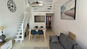 Un appartement moderne doté d’un escalier à la manière d’un loft, d’un coin repas avec une table ronde et des chaises, d’un canapé gris et d’une grande fenêtre ornée d’un tableau.