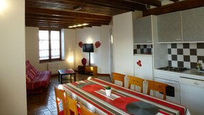 Uma sala de jantar com uma mesa posta para quatro pessoas, cadeiras de madeira, toalha xadrez vermelha e branca e uma televisão na parede.