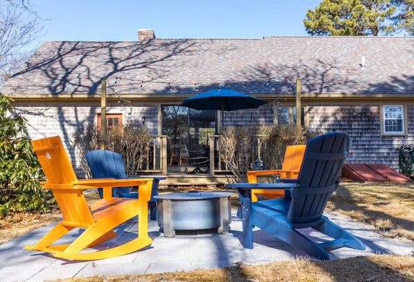 A patio with Adirondack chairs, a table, and a blue umbrella.