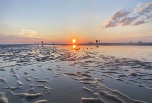 A beach at sunset with people walking and standing on the sand.
