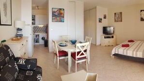 A hotel room with a bed, a TV, a dining table with chairs, a small kitchen area, and a bathroom.