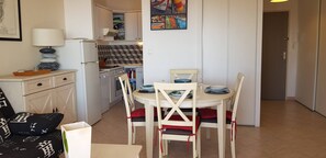 A compact kitchen with white cabinets, a refrigerator, a sink, and a dining area with a round table and chairs. - Large luxury studio by the sea (Ajaccio)