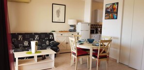 A compact living space with a sofa, dining table, chairs, a small kitchen area, and a framed artwork on the wall. - Large luxury studio by the sea (Ajaccio)