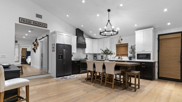 A modern kitchen with white cabinets, a black refrigerator, a dining area with a wooden table and chairs, and a chandelier. - Your Private Resort in SoCal Awaits (Long Beach)