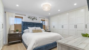 A bedroom with a large bed, a bedside table with a lamp, a wardrobe, and a hanging plant. - Your Private Resort in SoCal Awaits (Long Beach)
