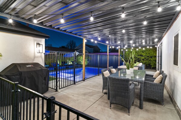 An outdoor patio with a covered seating area, a barbecue grill, and a swimming pool.