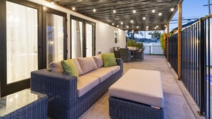 An outdoor covered patio area with a wicker sofa, a small table, and a bench. - Your Private Resort in SoCal Awaits (Long Beach)