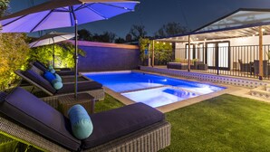 A backyard with a swimming pool, lounge chairs, and umbrellas. - Your Private Resort in SoCal Awaits (Long Beach)