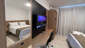 Una habitación de hotel con cama, escritorio con silla, televisor montado en la pared y ventana con cortinas.