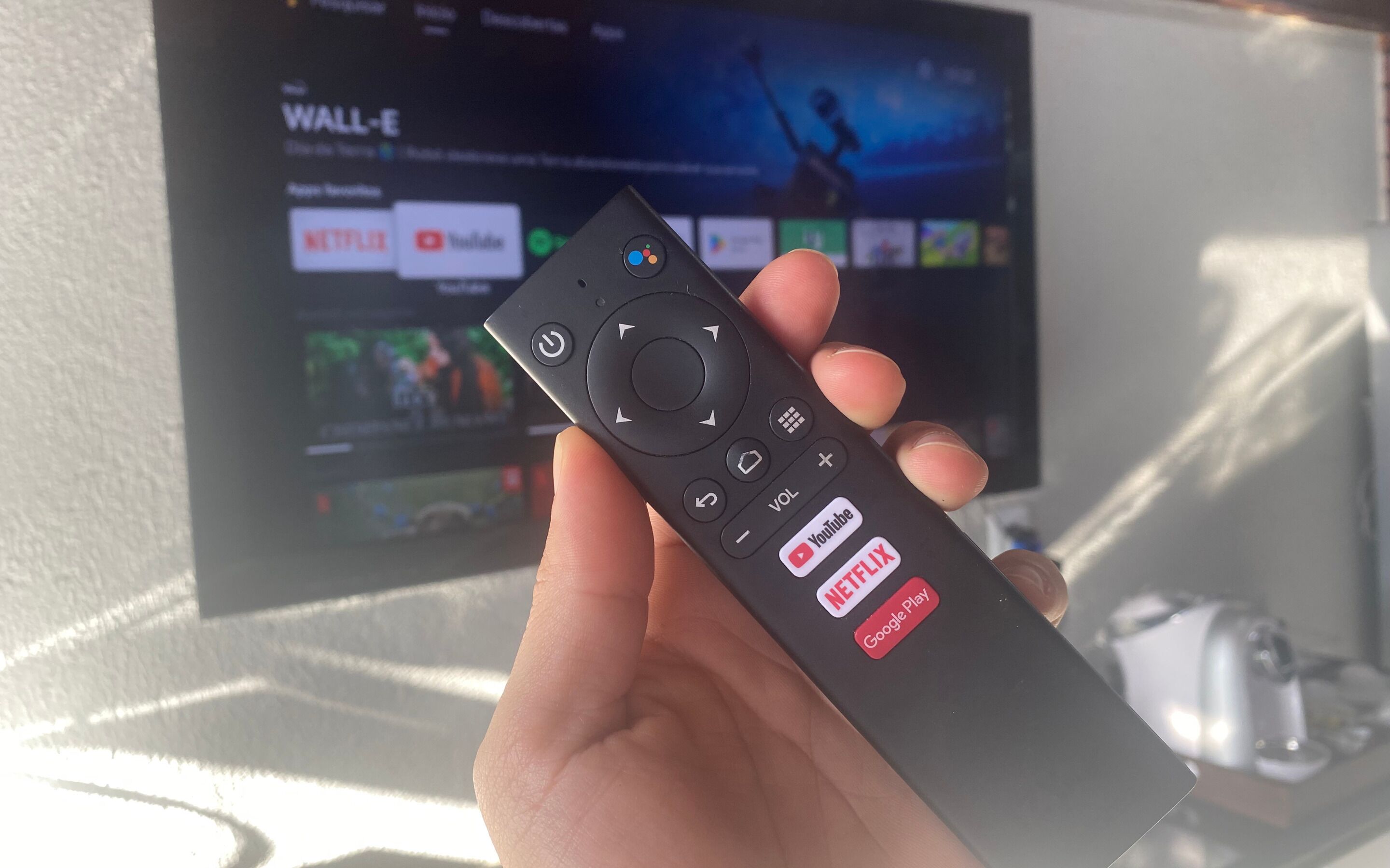 A hand holding a remote control with buttons for Netflix, YouTube, and Google Play.