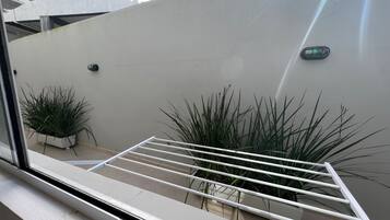 Una ventana con un estante metálico blanco, dos plantas en macetas y un aplique de pared.