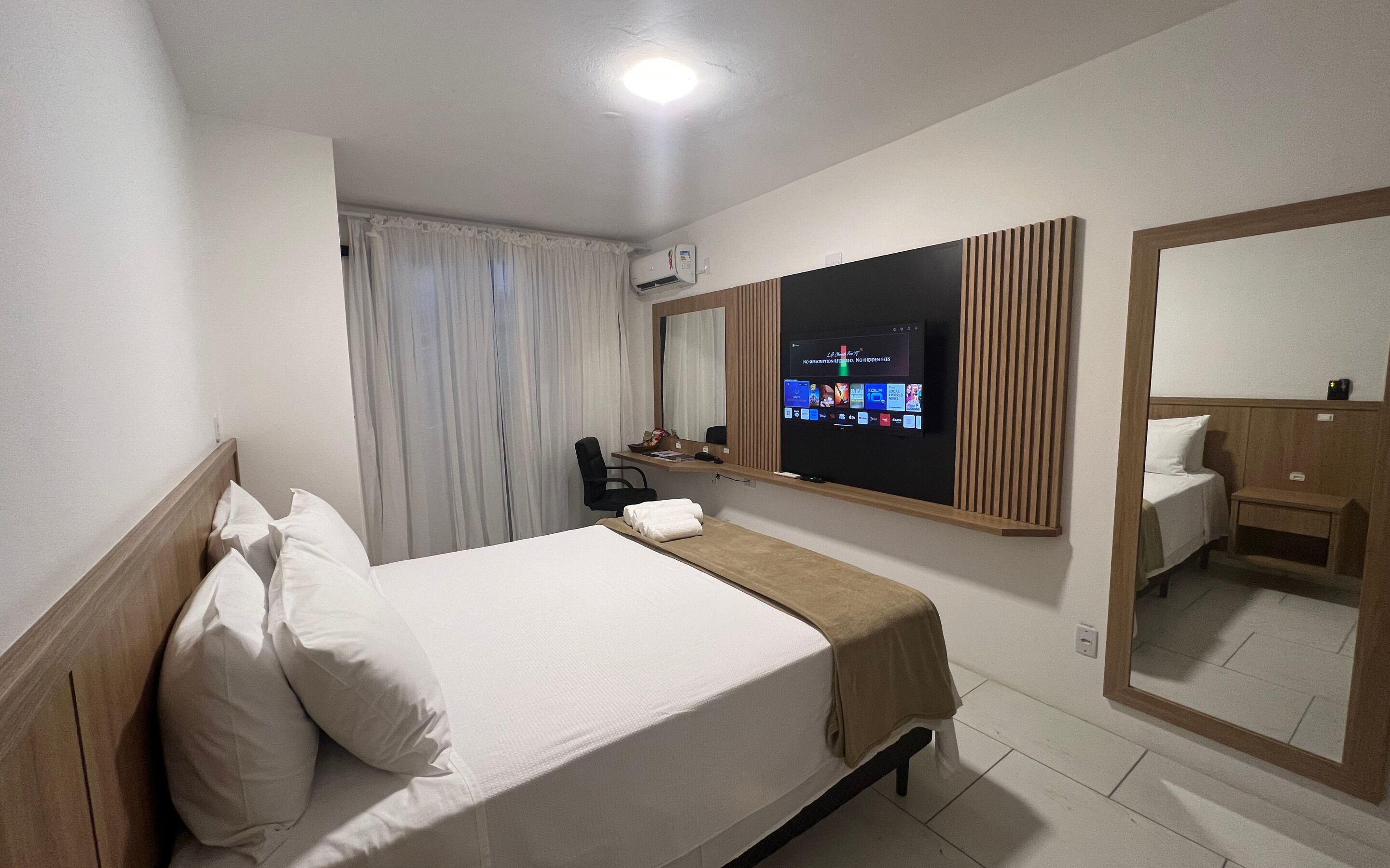 A hotel room with a bed, a desk, a TV, and a mirror.