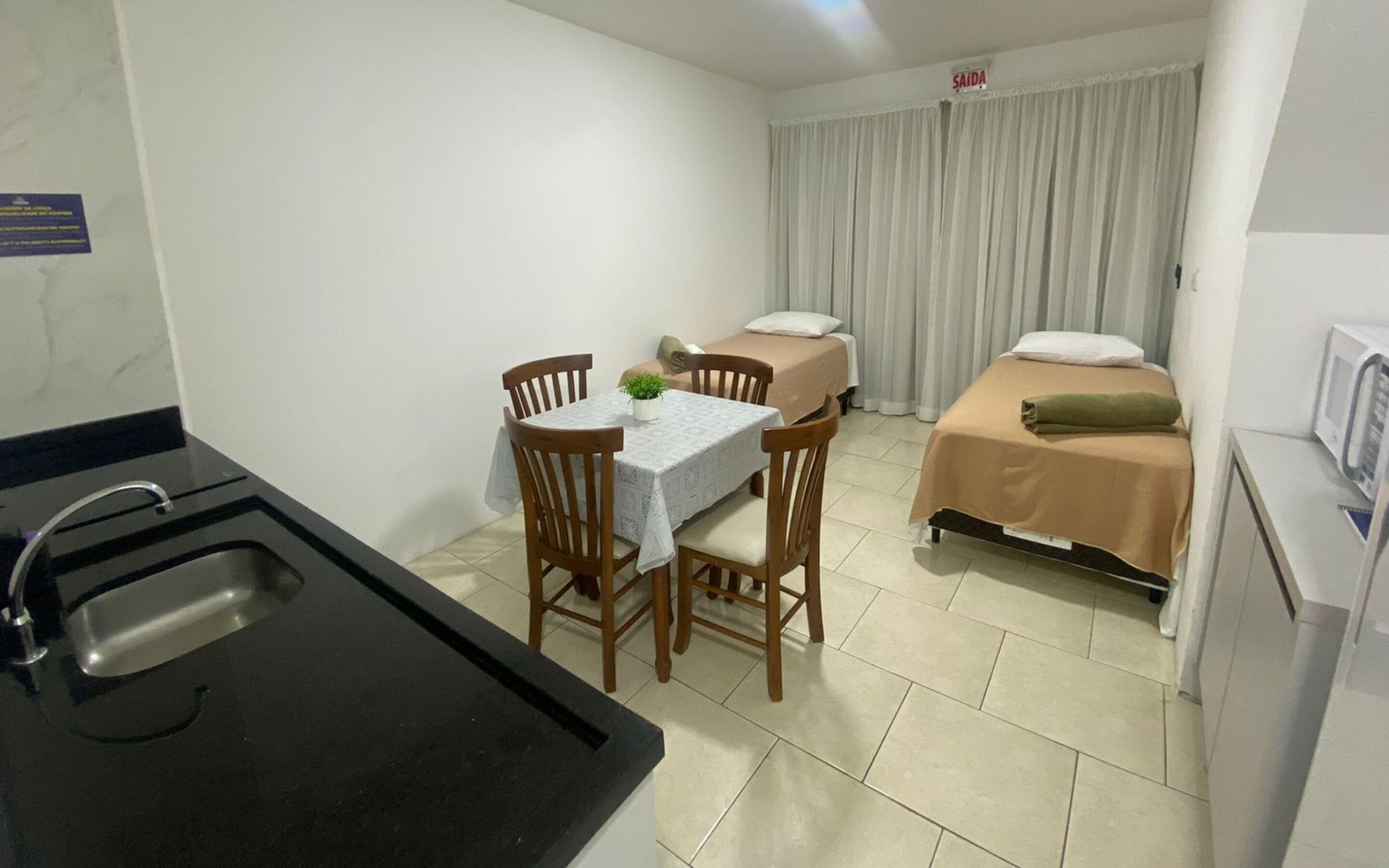 Een kleine hotelkamer met kitchenette, een eettafel met stoelen, een bed met een groen kussen en een badkamer met toilet en wastafel.