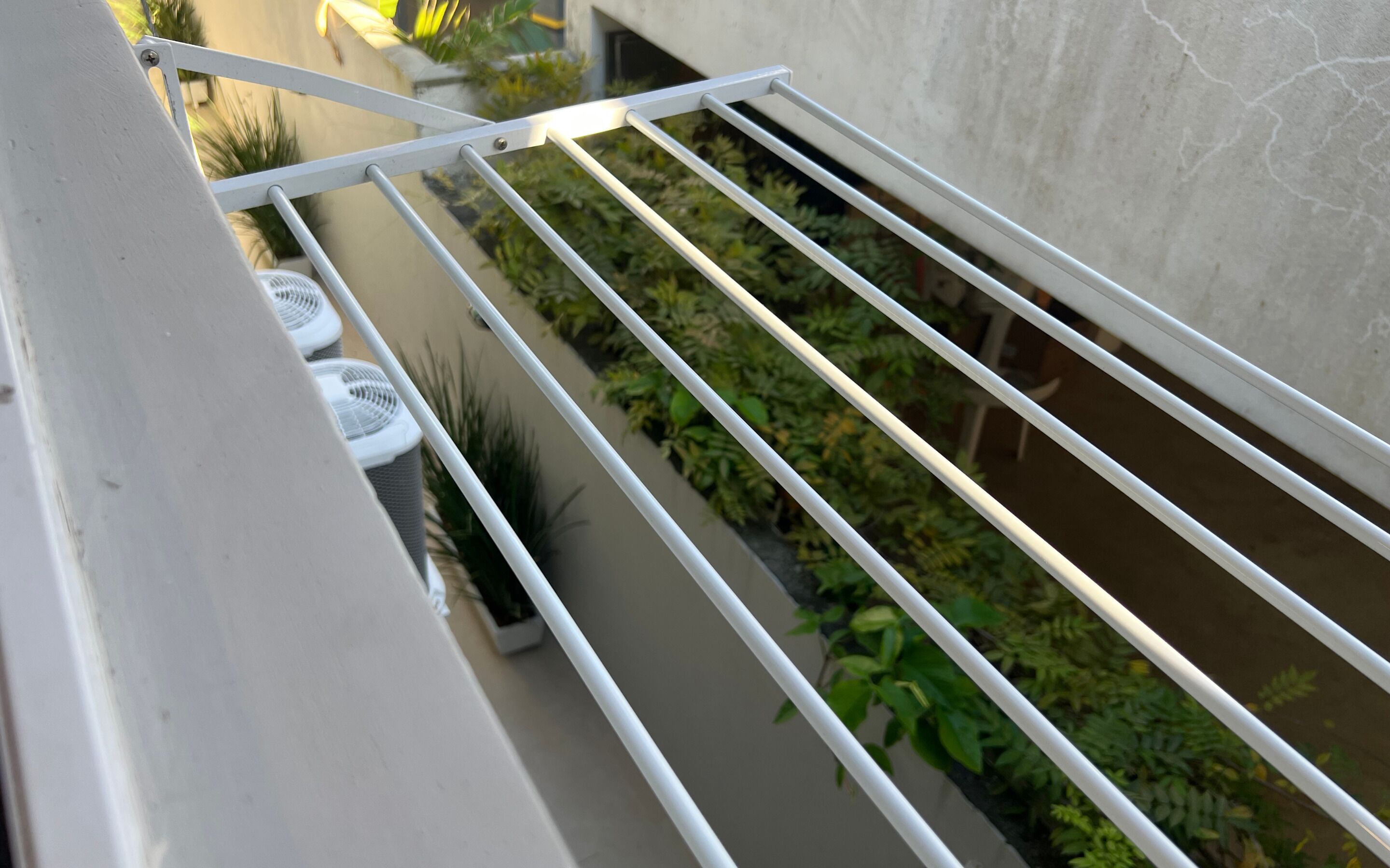 Un balcón con barandilla de metal, plantas en macetas y una pared blanca.