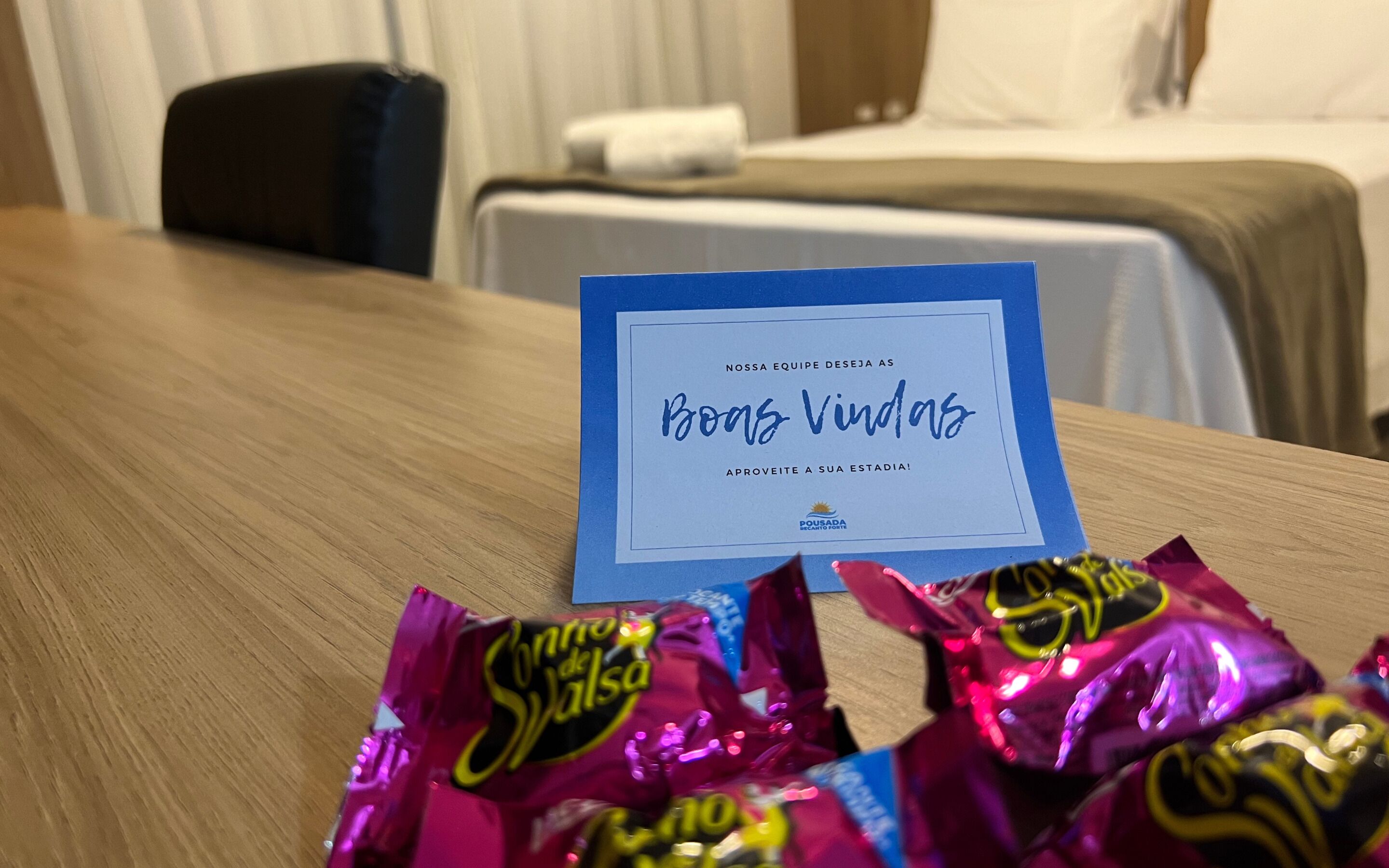 A hotel room with a wooden table, a card, and some wrapped chocolates.