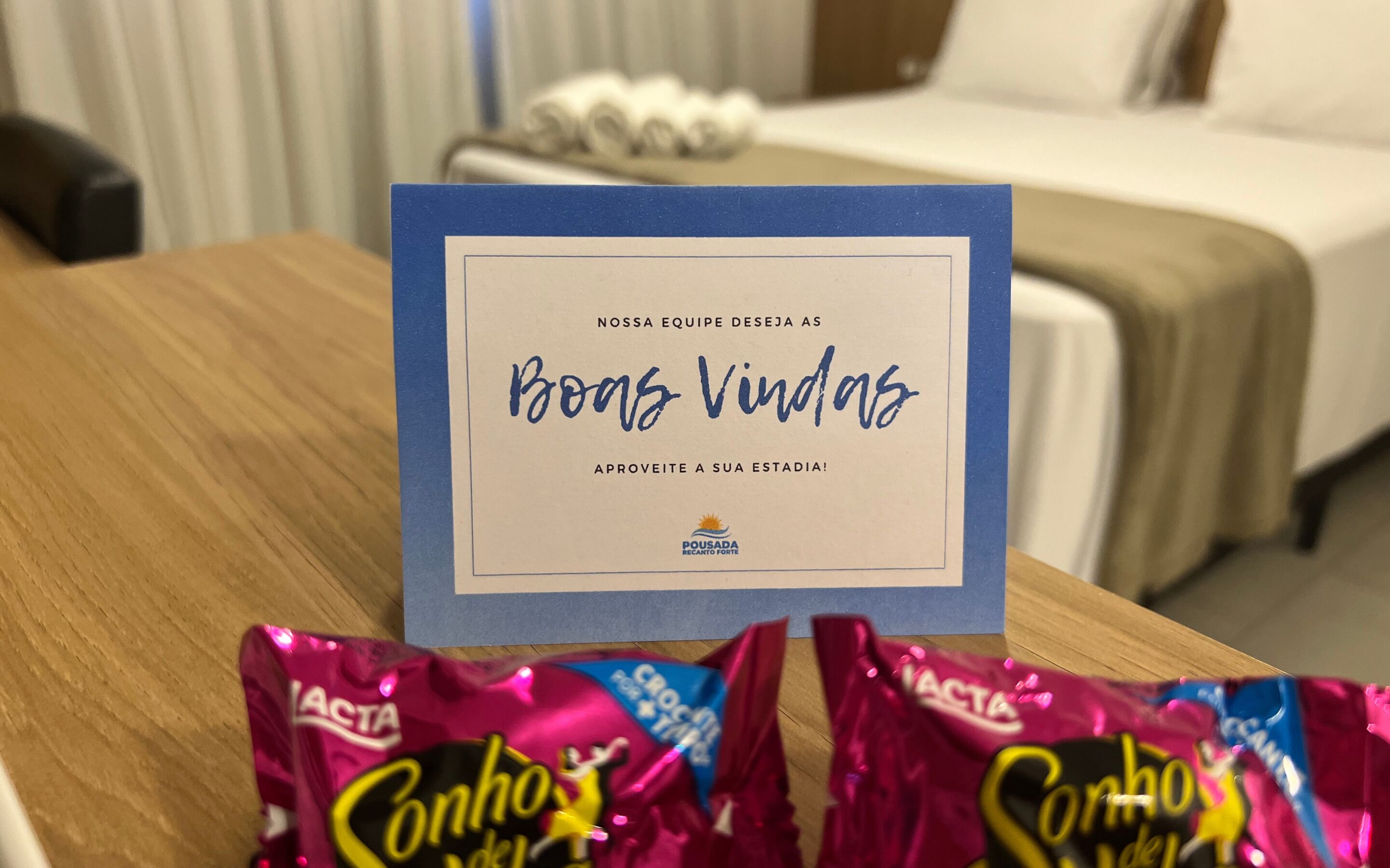 A hotel room with a bed, a bedside table, and a card on the table.