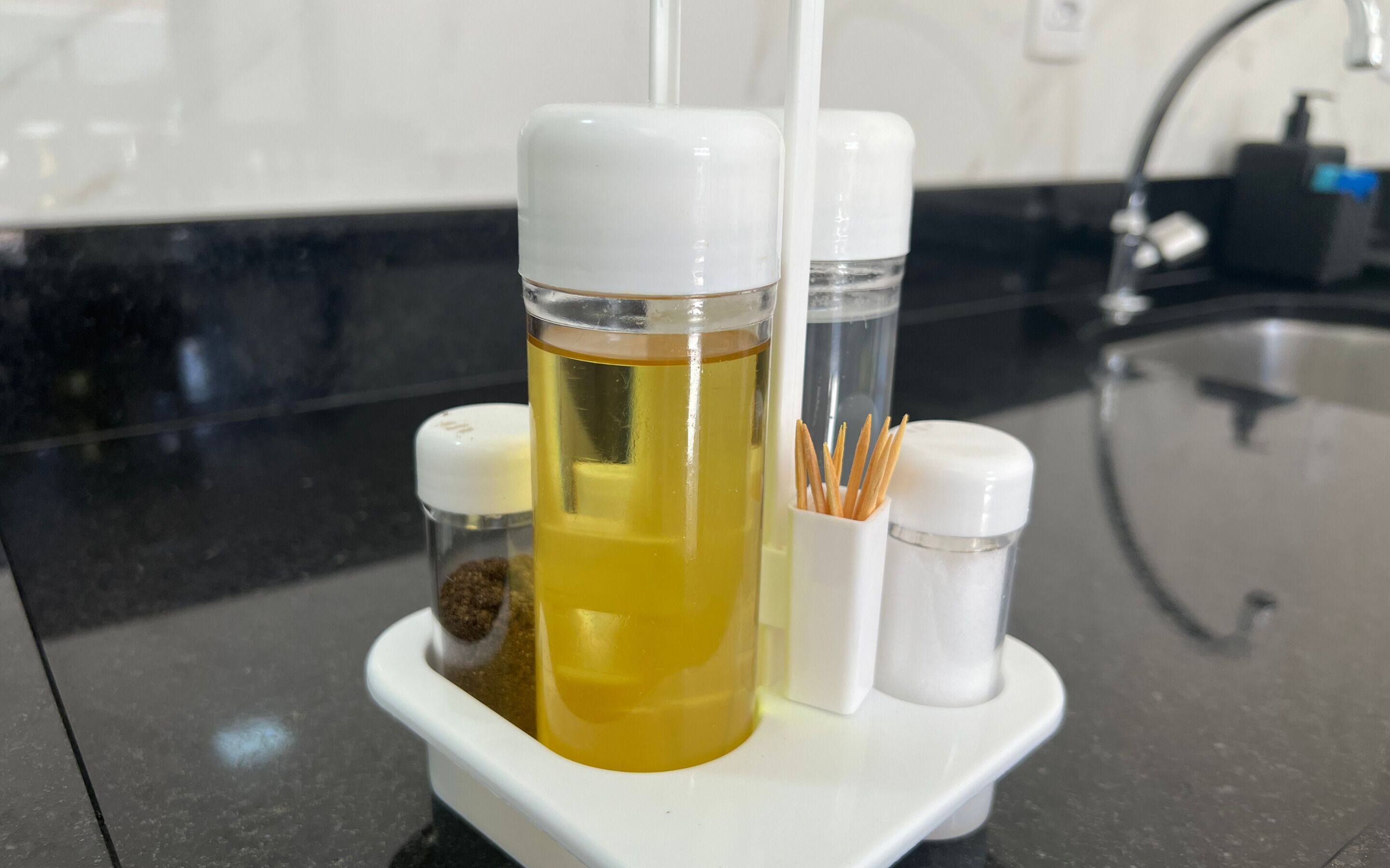 A kitchen counter with a white spice rack holding a bottle of yellow liquid, a salt shaker, and a pepper shaker.