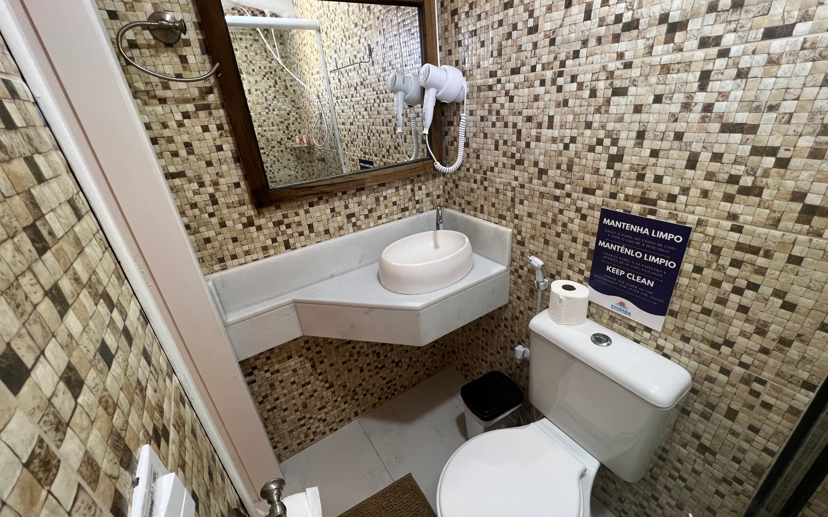 Un baño con pared de mosaicos, lavamanos, inodoro y secador de pelo.