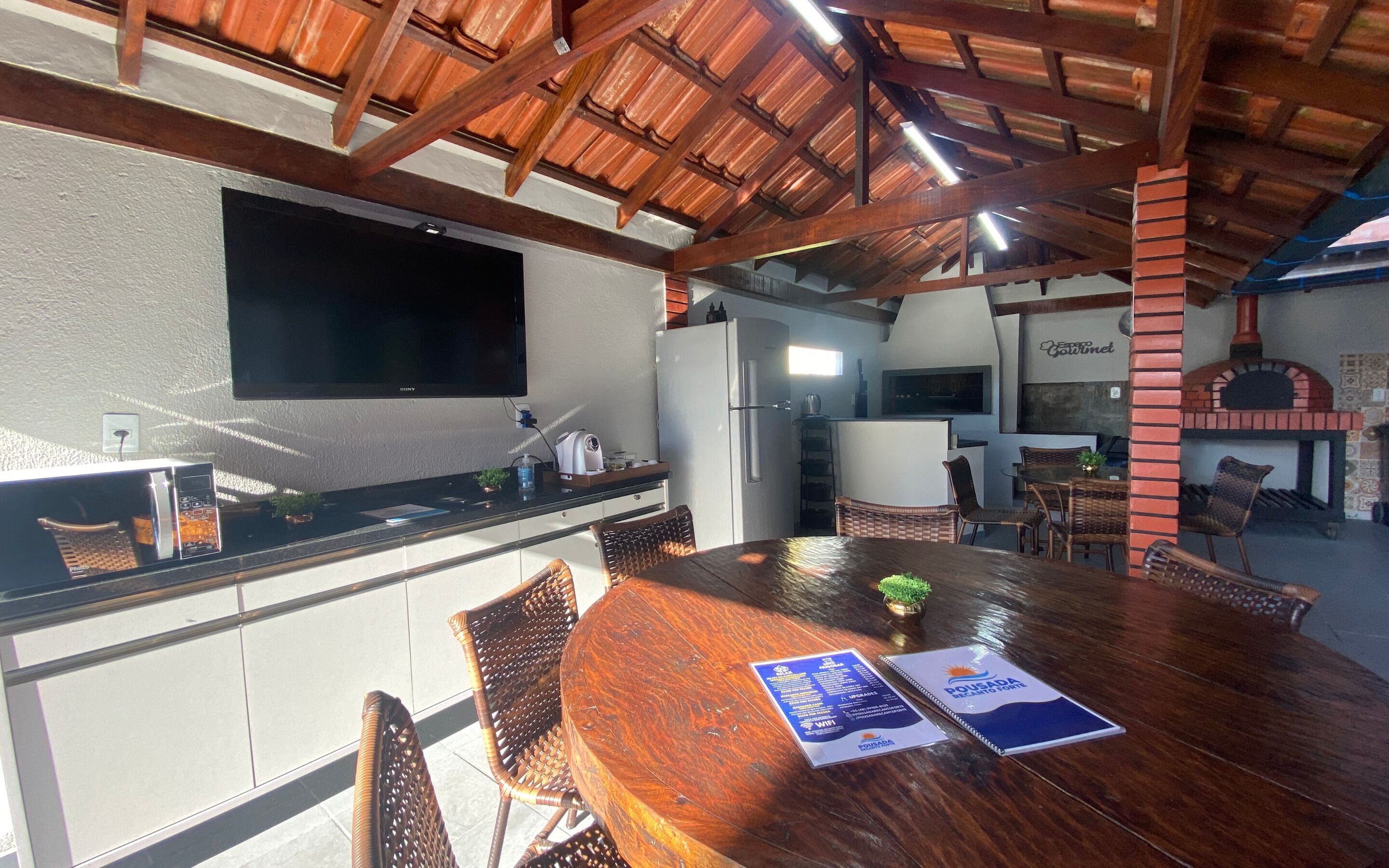 A kitchen with a wooden ceiling, a refrigerator, a microwave, and a dining area with wicker chairs and a wooden table.