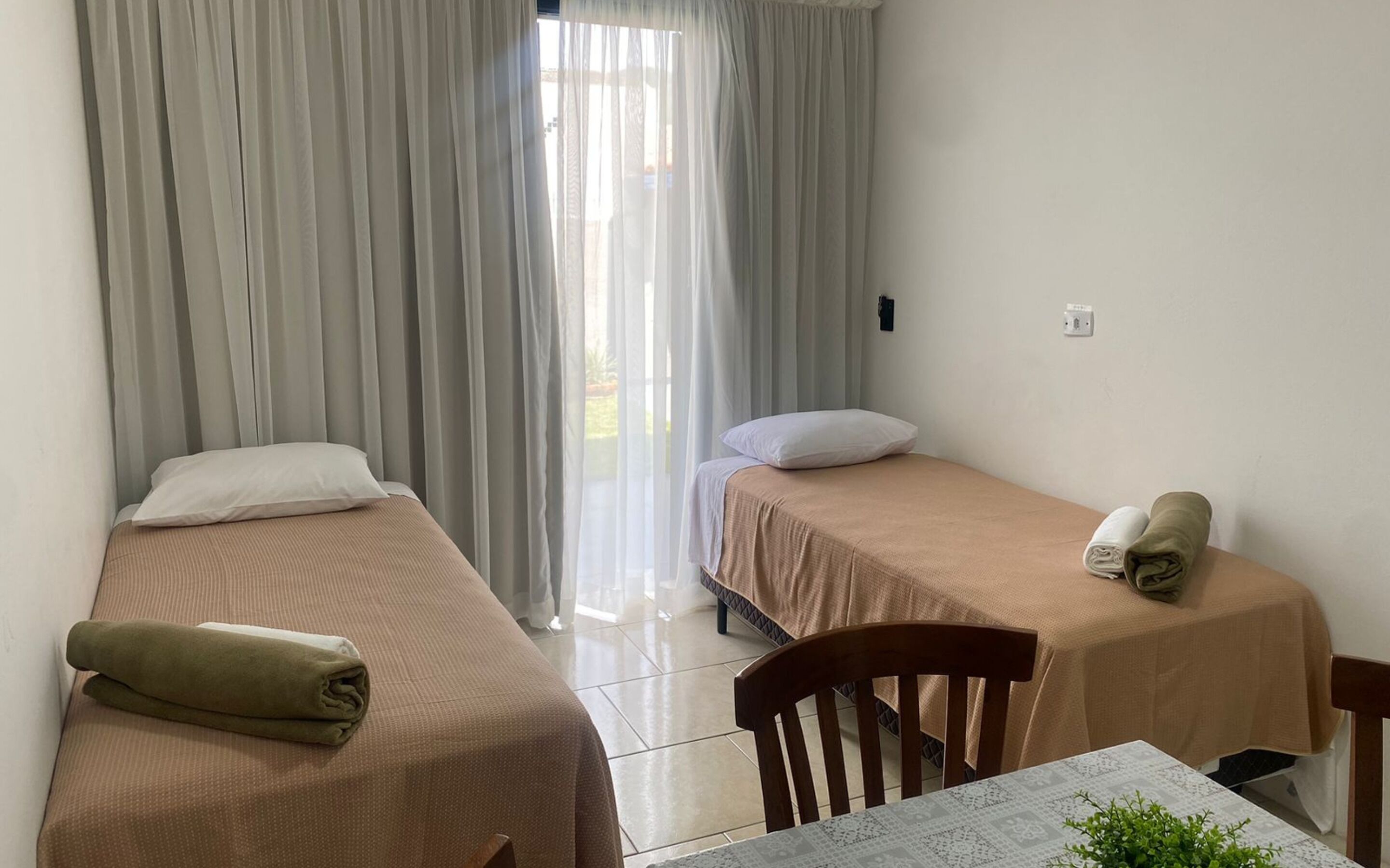A room with two single beds, a small table, and a chair.