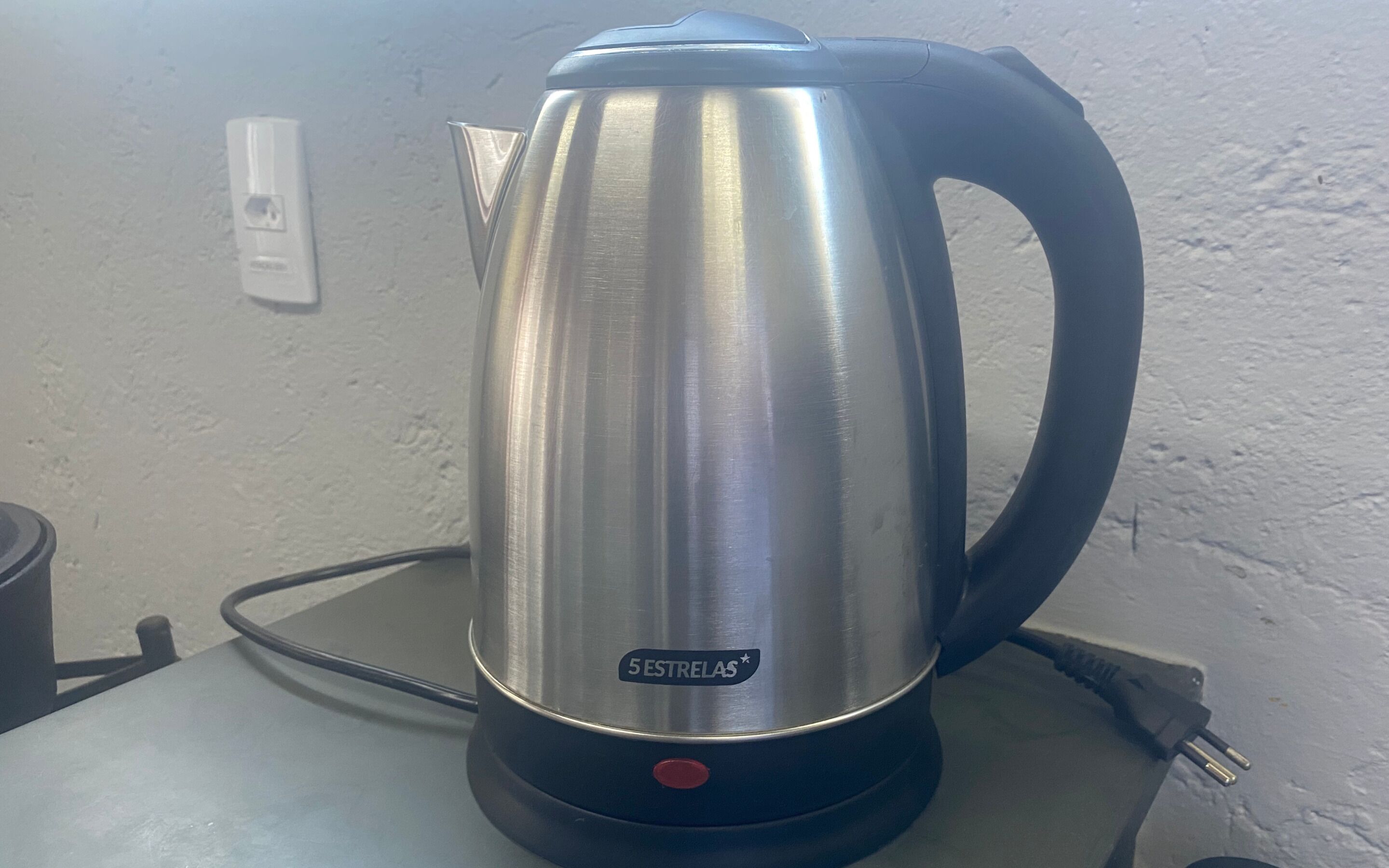 A stainless steel kettle with a black handle and base, labeled "5 Estrellas," on a countertop.