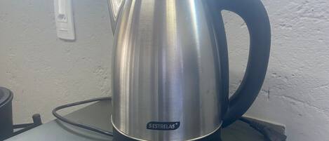 A stainless steel kettle with a black handle and base, labeled "5 Estrellas," on a countertop.