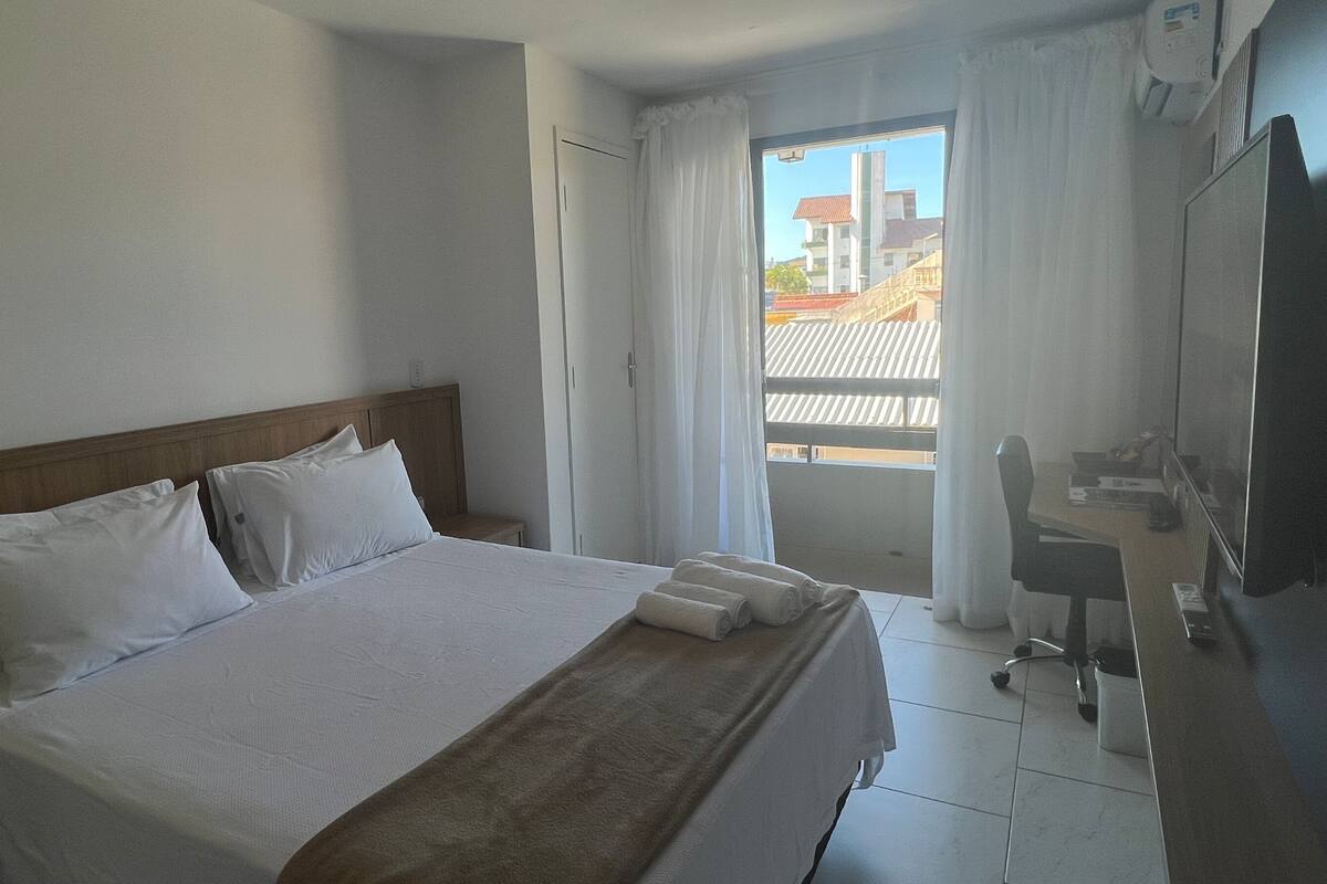 A hotel room with a bed, a desk, a chair, and a window with curtains.