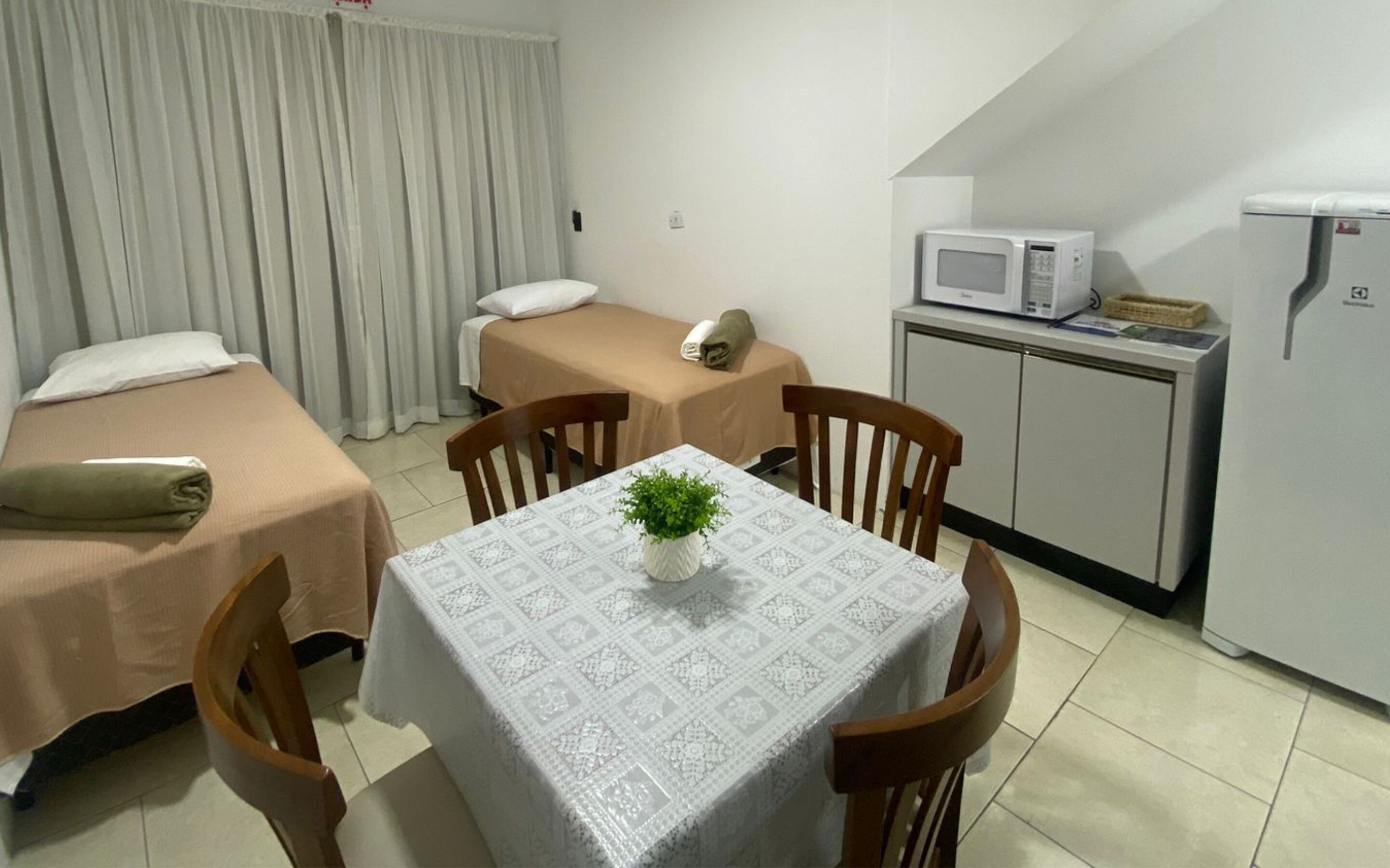 A small, clean room with two beds, a table with a plant, a microwave, and a refrigerator.
