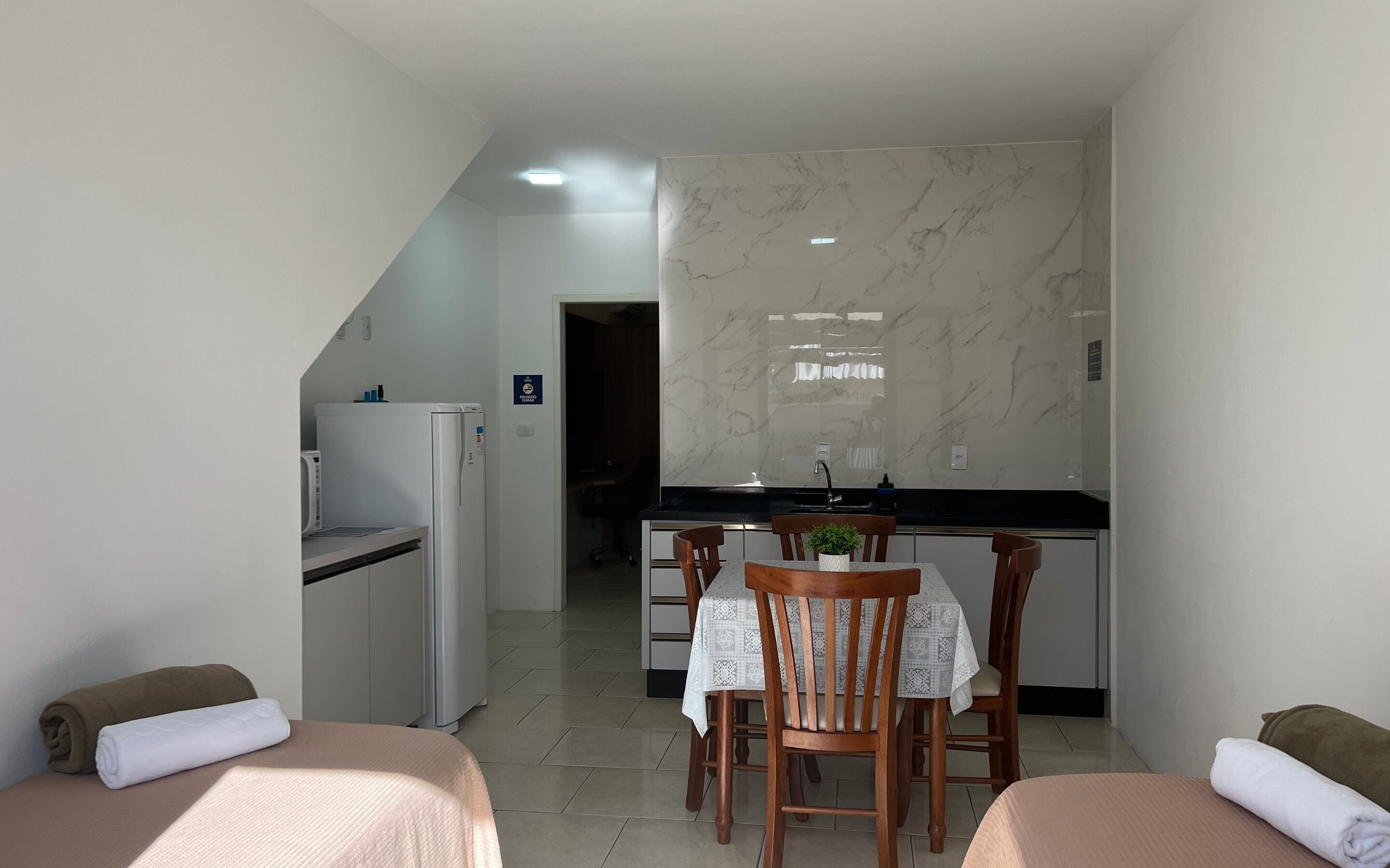 Habitación de hotel con kitchenette, zona de comedor con mesa y sillas, y dos camas con toallas.