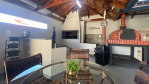 Una cocina con horno de ladrillo, sillas de mimbre, una mesa de vidrio y una cafetera.