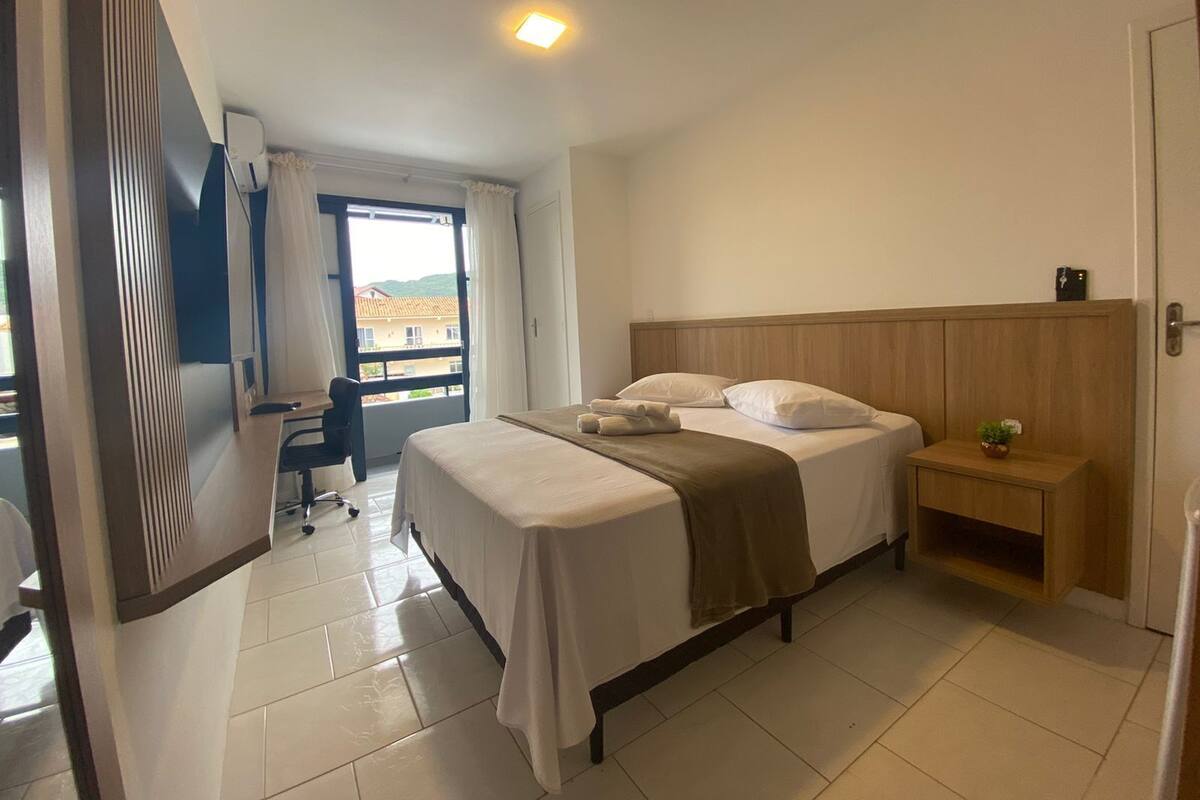 A hotel room with a bed, bedside table, and a view through a window.