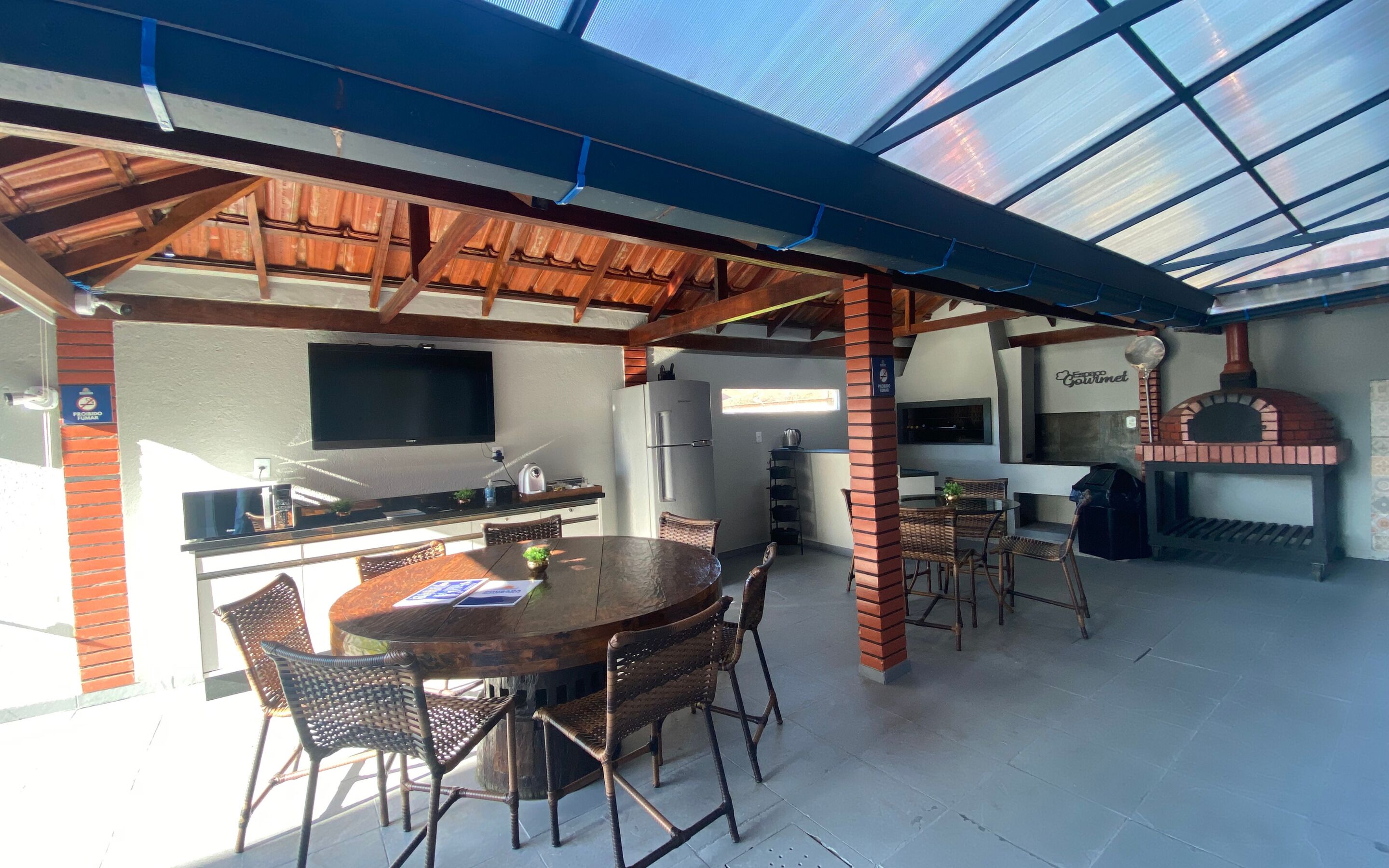Un espace cuisine extérieur comprenant un barbecue, une table à manger avec des chaises et un téléviseur fixé au mur.