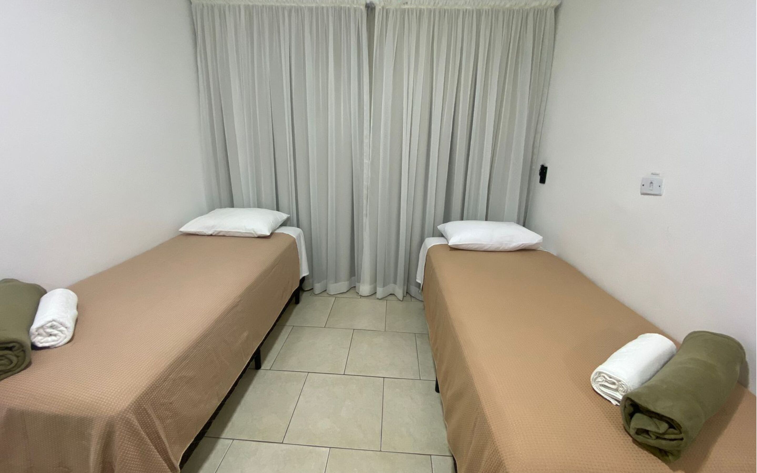 A room with two single beds, each with a pillow and a rolled towel.